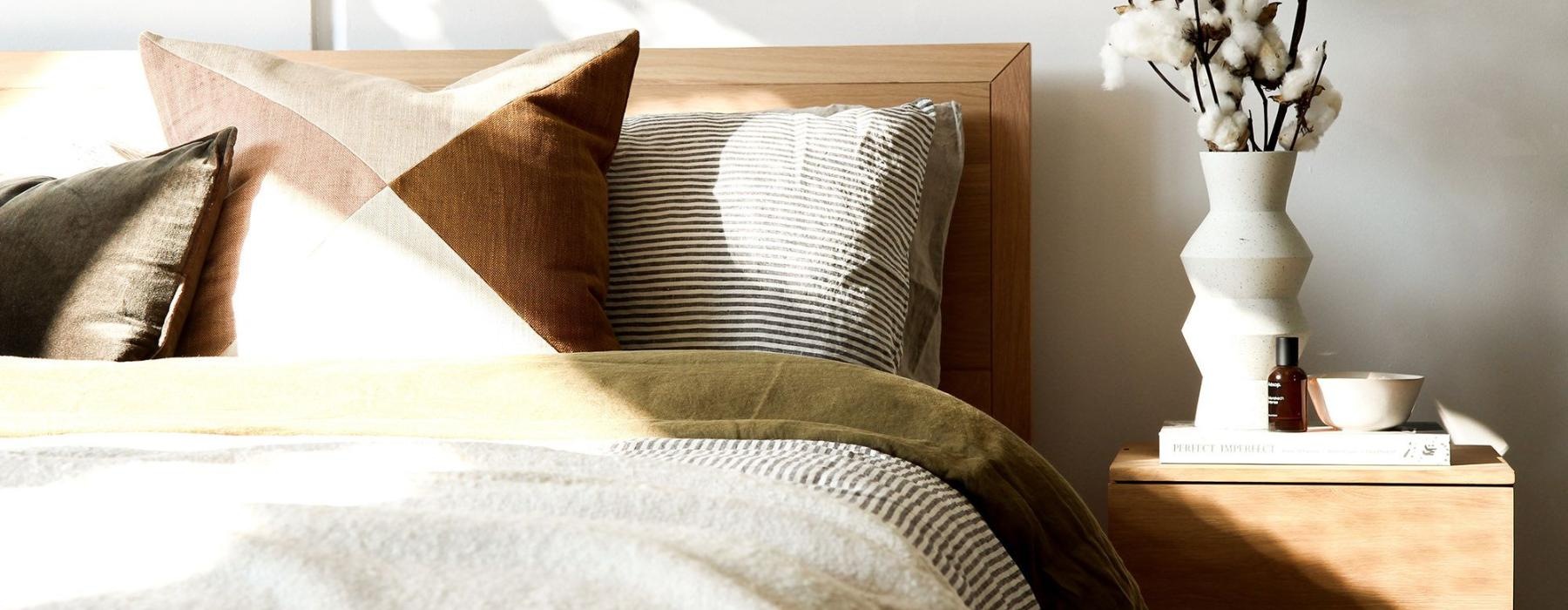 swath of sunlight shines across a well made bed and bedside table with a vase of cotton plants